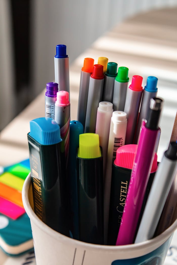 Close-up of a cup filled with vibrant pens and markers on a desk.