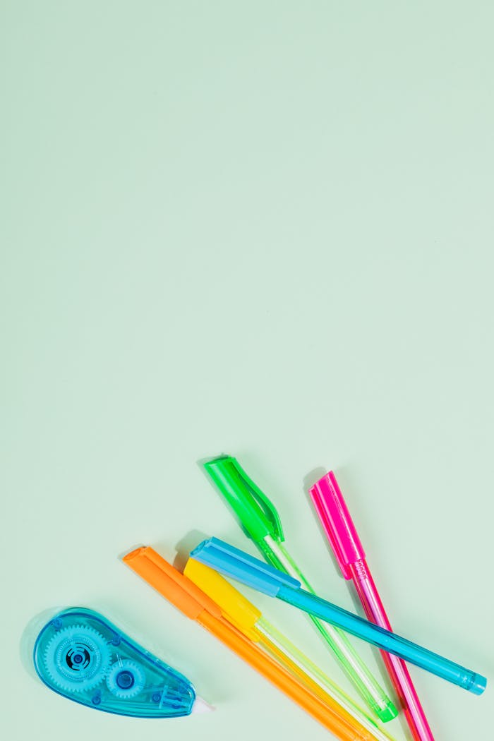 Assorted school supplies including pens and correction tape on a green backdrop.
