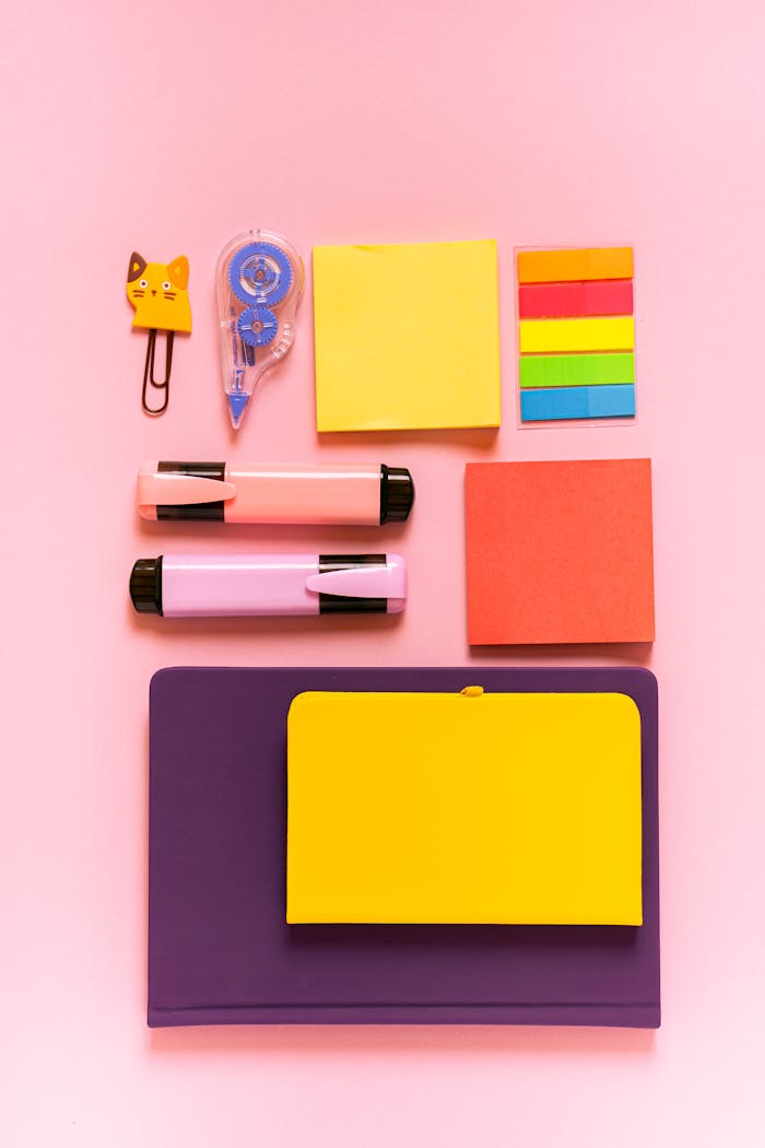 An aesthetically pleasing arrangement of colorful stationery items on a pink background.