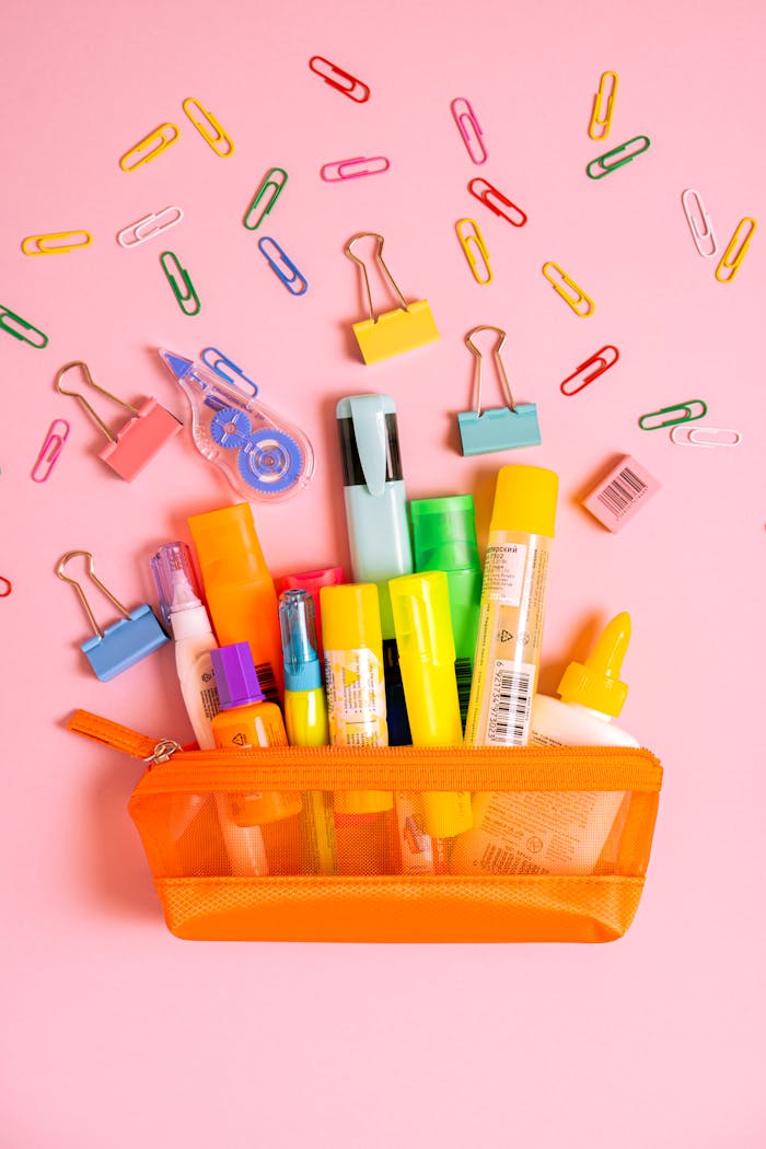 Vibrant desk supplies spilling from an orange pouch on a pink backdrop.