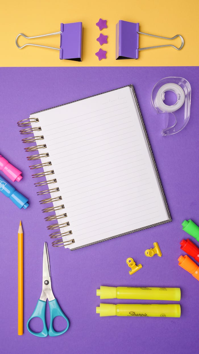 Top view of a spiral notebook with colorful stationery items on a vibrant background.