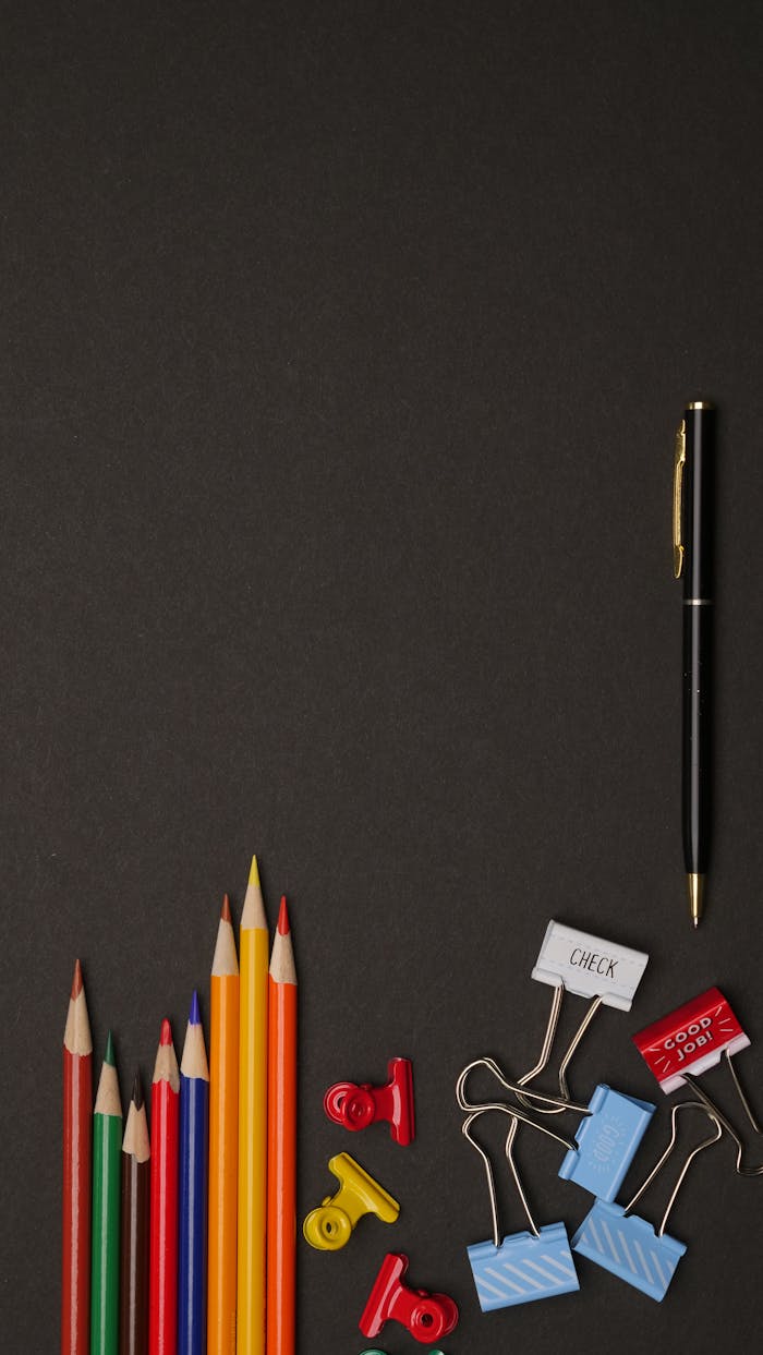 A collection of colorful pencils and clips on a dark background with ample copy space.