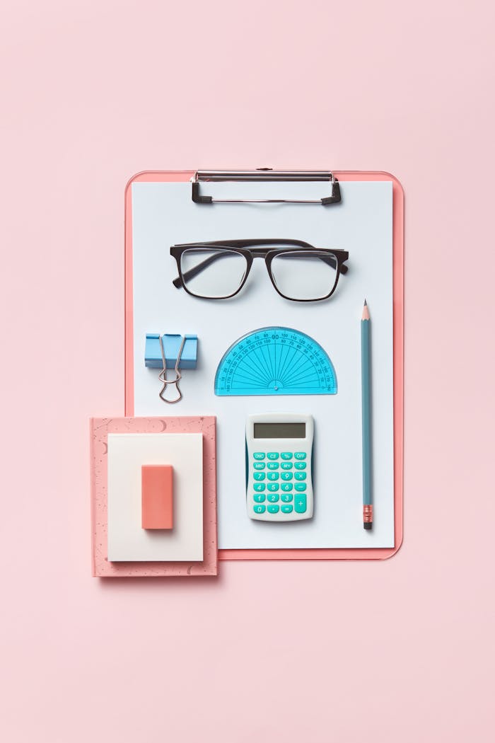 Modern flat lay featuring office supplies like calculator, clipboard, and glasses on a pink surface.
